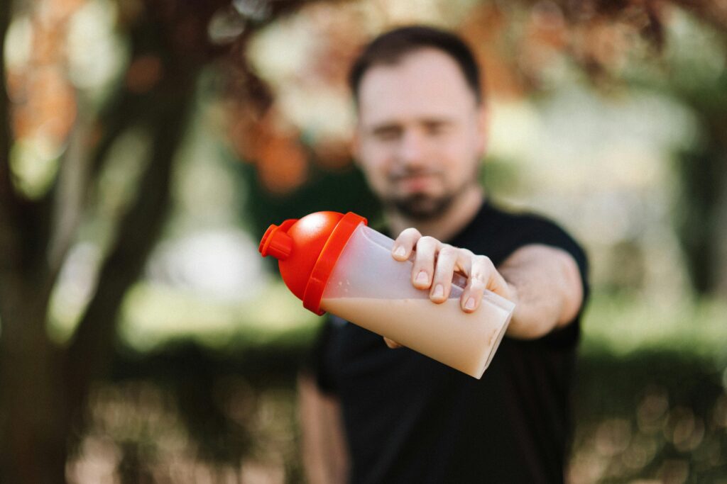 Protein-Packed Snacks on the Go: Shake it Up! Man presenting a protein shake in a plastic tumbler against a blurred nature background.