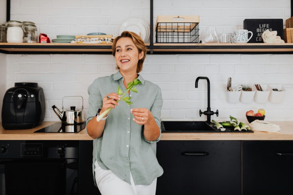 Quick Healthy Meals in the Air Fryer Smiling woman with vegetables in a stylish kitchen showcasing modern interior design.