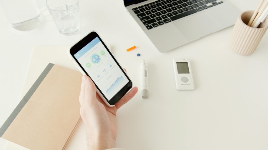 Portable Wellness Tech for Healthier Living A person checks glucose levels on a smartphone app next to diabetes monitoring equipment.