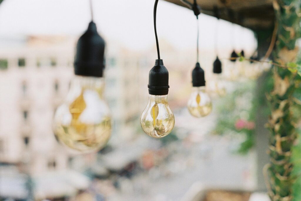 A row of hanging string light bulbs against a blurred cityscape background.