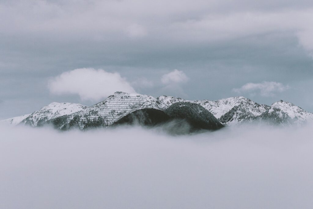 A serene winter view of snow-capped mountains rising above misty clouds on a cloudy day.