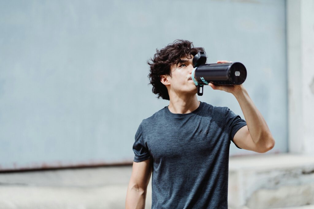 Stay Hydrated with Smart Bottles: Your Guide to Daily Hydration Man in a casual outfit drinking water from a bottle outdoors, focused on fitness and hydration.