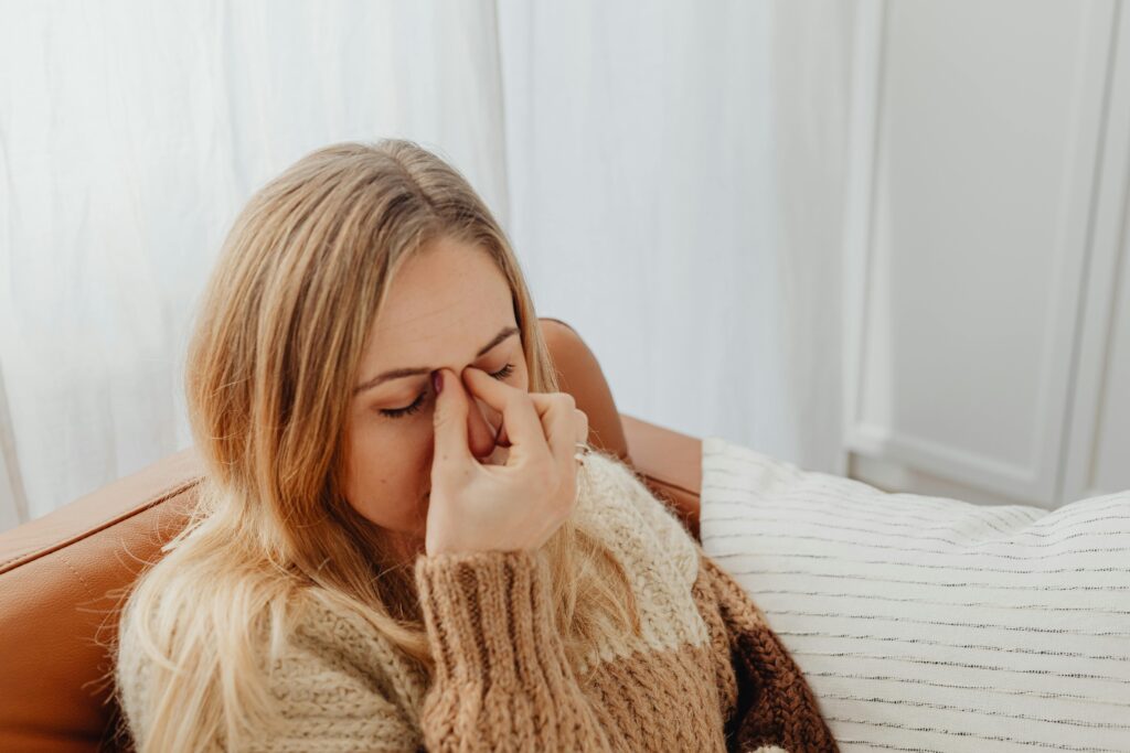 A woman sitting on a couch with eyes closed, holding her nose in apparent sinus pain.